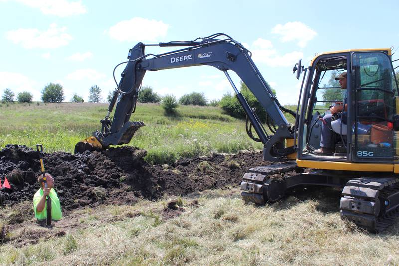 Correy Rahn moves dirt back into the trench after laying new tile while Mitchel Rahn (in trench) assists with the process. Once the larger diameter tile is put into place, the farmers will use their tile plow to lay the pattern tile in the field.